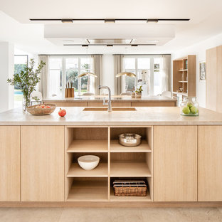 Modelo de cocinas en U contemporáneo, de tamaño medio, abierto, con armarios con paneles lisos, puertas de armario de madera clara, electrodomésticos negros, dos o más islas, suelo beige y encimeras beige