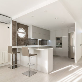 Foto de cocina en U, actual, con puertas de armario grises, suelo de madera clara, península, encimeras blancas, armarios con paneles lisos, salpicadero marrón, electrodomésticos de acero inoxidable y suelo gris