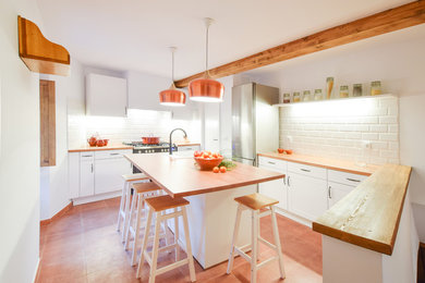 マドリードにある中くらいな地中海スタイルのおしゃれなキッチン (レイズドパネル扉のキャビネット、白いキャビネット、木材カウンター、白いキッチンパネル、サブウェイタイルのキッチンパネル、シルバーの調理設備、赤い床) の写真