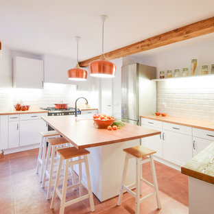 Foto de cocina comedor en U, mediterránea, de tamaño medio, con armarios con paneles con relieve, puertas de armario blancas, encimera de madera, salpicadero blanco, salpicadero de azulejos tipo metro, electrodomésticos de acero inoxidable, una isla y suelo rojo