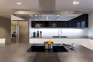 Große Moderne Wohnküche in U-Form mit Doppelwaschbecken, flächenbündigen Schrankfronten, weißen Schränken, Küchengeräten aus Edelstahl, braunem Holzboden und Kücheninsel in Barcelona