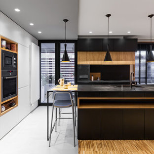 Modelo de cocina de galera, minimalista, grande, abierta, con fregadero bajoencimera, armarios con paneles lisos, puertas de armario negras, encimera de granito, electrodomésticos con paneles, suelo de madera en tonos medios, una isla, suelo marrón y encimeras negras