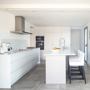Imagen de cocina lineal, mediterránea, grande, cerrada, con fregadero bajoencimera, armarios con paneles lisos, puertas de armario blancas, encimera de cuarzo compacto, salpicadero blanco, salpicadero de vidrio, electrodomésticos con paneles, suelo de baldosas de cerámica, una isla, suelo gris y encimeras blancas