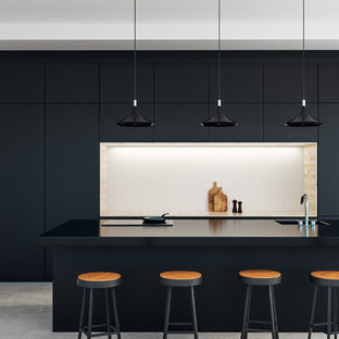 Modelo de cocina de galera, contemporánea, abierta, con encimeras negras, fregadero integrado, armarios con paneles lisos, puertas de armario negras, electrodomésticos negros, suelo de cemento, una isla y suelo gris