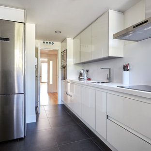 Diseño de cocina lineal, moderna, de tamaño medio, cerrada, sin isla, con armarios con paneles lisos, puertas de armario blancas, salpicadero blanco, electrodomésticos de acero inoxidable, encimeras blancas, fregadero bajoencimera, suelo negro y suelo de cemento