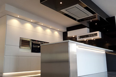 Ejemplo de cocina moderna de tamaño medio con armarios con paneles lisos, puertas de armario blancas, electrodomésticos de acero inoxidable y península