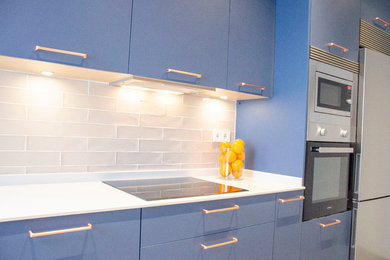 Imagen de cocina lineal de tamaño medio cerrada sin isla con puertas de armario azules, encimera de cuarzo compacto y encimeras blancas