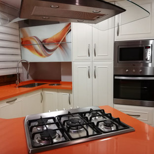 Modelo de cocina comedor en U, tradicional, pequeña, con fregadero bajoencimera, armarios con rebordes decorativos, puertas de armario blancas, encimera de cuarzo compacto, electrodomésticos de acero inoxidable, suelo de terrazo, península, suelo multicolor y encimeras naranjas