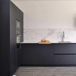 Modelo de cocina en L, minimalista, sin isla, con armarios con paneles lisos, puertas de armario negras, salpicadero blanco, encimeras blancas, fregadero de un seno, electrodomésticos con paneles y suelo gris