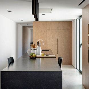 Foto de cocina contemporánea, abierta, con fregadero de un seno, armarios con paneles lisos, puertas de armario de madera en tonos medios, encimera de granito, electrodomésticos negros, suelo de baldosas de porcelana, una isla, suelo gris y encimeras negras