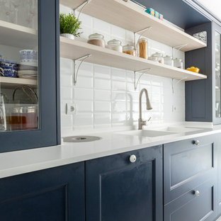 Diseño de cocina clásica renovada con puertas de armario azules, salpicadero blanco, encimeras blancas, fregadero de doble seno y armarios tipo vitrina