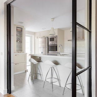 Foto de cocina clásica renovada, cerrada, con armarios estilo shaker, puertas de armario beige, suelo gris, encimeras blancas, fregadero bajoencimera, salpicadero blanco y electrodomésticos de acero inoxidable