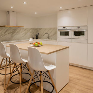 Modelo de cocina en L, contemporánea, con armarios con paneles lisos, puertas de armario blancas, una isla, fregadero bajoencimera, encimera de madera, salpicadero verde, electrodomésticos blancos, suelo de madera clara, suelo marrón y encimeras beige