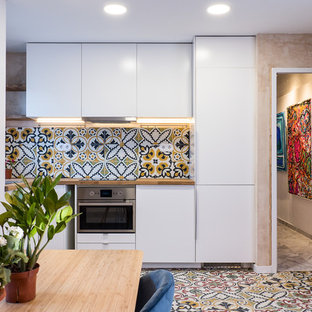 Diseño de cocina comedor en L, actual, pequeña, sin isla, con armarios con paneles lisos, puertas de armario blancas, encimera de madera, electrodomésticos de acero inoxidable, fregadero encastrado, salpicadero multicolor, suelo multicolor y encimeras beige