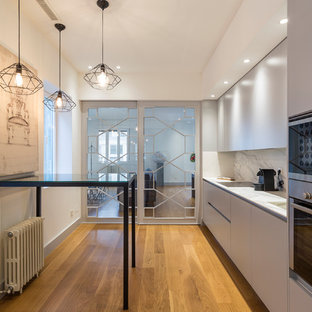 Modelo de cocina lineal, contemporánea, de tamaño medio, con armarios con paneles lisos, puertas de armario grises, encimera de mármol, salpicadero blanco, salpicadero de mármol, electrodomésticos de acero inoxidable, suelo de madera en tonos medios y encimeras blancas