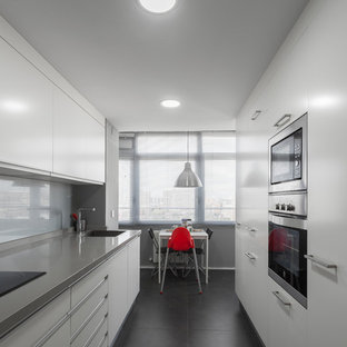 Modelo de cocina de galera, actual, cerrada, sin isla, con fregadero de un seno, armarios con paneles lisos, puertas de armario blancas, salpicadero verde, salpicadero de vidrio templado, electrodomésticos negros, suelo negro y encimeras grises