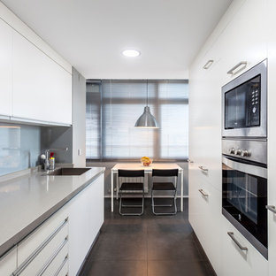 Diseño de cocina de galera, actual, grande, cerrada, sin isla, con fregadero bajoencimera, armarios con paneles lisos, puertas de armario blancas, electrodomésticos de acero inoxidable, suelo gris, encimeras grises, salpicadero verde y salpicadero de vidrio templado