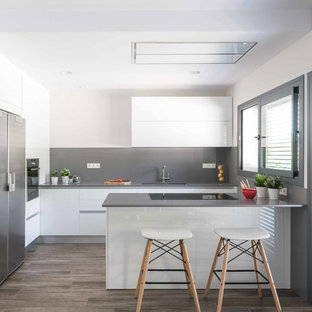 Diseño de cocina contemporánea con armarios con paneles lisos, puertas de armario blancas, salpicadero verde, electrodomésticos de acero inoxidable, suelo de madera oscura, península, encimeras grises, fregadero de doble seno y suelo marrón