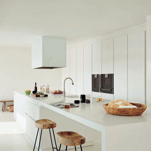 Large contemporary galley kitchen in Madrid with an integrated sink, flat-panel cabinets, white cabinets, solid surface benchtops, with island, black appliances and white benchtop.