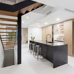 Imagen de cocina lineal, minimalista, con armarios con paneles lisos, una isla, encimeras negras, fregadero de un seno, puertas de armario de madera clara y suelo blanco