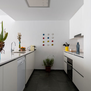 Foto de cocina de galera, actual, de tamaño medio, con fregadero bajoencimera, armarios con paneles lisos, puertas de armario blancas, salpicadero blanco, electrodomésticos con paneles, suelo de baldosas de porcelana, península, suelo negro y encimeras blancas