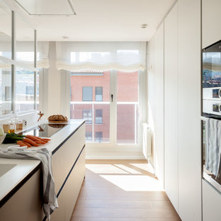 Ejemplo de cocina de galera, contemporánea, sin isla, con fregadero bajoencimera, armarios con paneles lisos, puertas de armario blancas, electrodomésticos de acero inoxidable, suelo de madera en tonos medios, suelo marrón y encimeras blancas