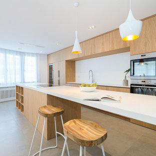 Imagen de cocina de galera, actual, con fregadero integrado, armarios con paneles lisos, puertas de armario de madera clara, salpicadero blanco, electrodomésticos de acero inoxidable, una isla, suelo gris y encimeras blancas