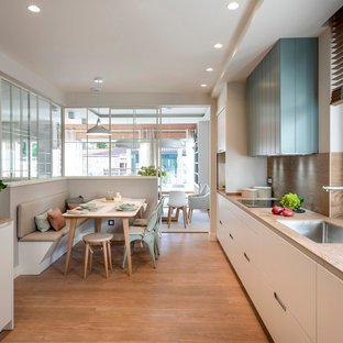 Modelo de cocina lineal, nórdica, grande, abierta, sin isla, con fregadero bajoencimera, armarios con paneles empotrados, puertas de armario blancas, encimera de cuarzo compacto, salpicadero marrón, salpicadero de azulejos de cerámica, electrodomésticos con paneles, suelo laminado, suelo marrón y encimeras marrones