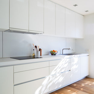 Diseño de cocina lineal, minimalista, de tamaño medio, abierta, sin isla, con armarios con paneles lisos, puertas de armario blancas, salpicadero blanco, suelo de madera en tonos medios, electrodomésticos de acero inoxidable, fregadero de un seno, encimera de laminado y suelo marrón