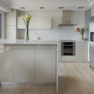 Imagen de cocina comedor contemporánea con armarios con paneles lisos, puertas de armario beige, salpicadero verde, electrodomésticos de acero inoxidable, suelo de madera clara, suelo beige y encimeras blancas