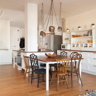 Modelo de cocina en U, clásica renovada, abierta, con armarios estilo shaker, puertas de armario blancas, encimera de madera, electrodomésticos de acero inoxidable, suelo de madera clara, una isla, suelo beige y encimeras marrones