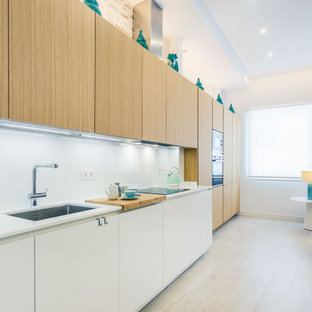 Modelo de cocina lineal, actual, abierta, sin isla, con fregadero bajoencimera, armarios con paneles lisos, puertas de armario de madera clara, electrodomésticos de acero inoxidable, suelo de madera clara, suelo beige y encimeras blancas