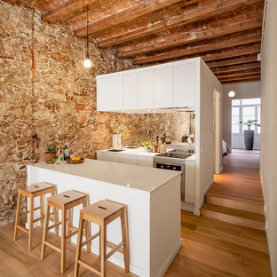 Foto de cocina de galera, actual, de tamaño medio, abierta, con armarios con paneles lisos, puertas de armario blancas, península, fregadero bajoencimera, salpicadero con efecto espejo, electrodomésticos de acero inoxidable, suelo de madera en tonos medios y suelo marrón