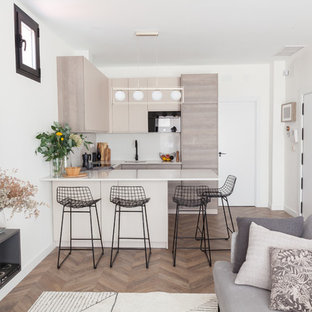 Photo of a mid-sized scandinavian u-shaped open plan kitchen in Madrid with an undermount sink, flat-panel cabinets, beige cabinets, quartz benchtops, beige splashback, limestone splashback, black appliances, laminate floors, a peninsula, brown floor and beige benchtop.