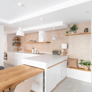 Diseño de cocina comedor en L, nórdica, con fregadero bajoencimera, armarios con paneles lisos, puertas de armario blancas, salpicadero beige, electrodomésticos de acero inoxidable, península, suelo gris y encimeras blancas
