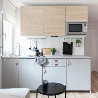 Imagen de cocina lineal, nórdica, pequeña, abierta, sin isla, con fregadero encastrado, armarios con paneles lisos, puertas de armario de madera clara, encimera de laminado, salpicadero blanco, salpicadero de vidrio, electrodomésticos de acero inoxidable, suelo laminado, suelo marrón y encimeras grises