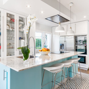 Foto de cocina en L, clásica renovada, con puertas de armario azules, electrodomésticos de acero inoxidable, una isla, fregadero encastrado, armarios estilo shaker y suelo de madera clara