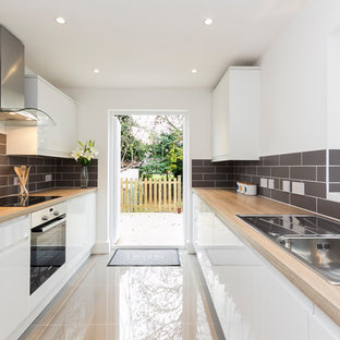 Modelo de cocina lineal, actual, con fregadero sobremueble, armarios con paneles lisos, puertas de armario blancas, encimera de madera, salpicadero verde y electrodomésticos de acero inoxidable