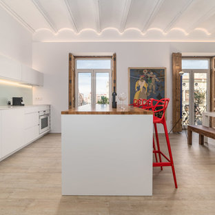 Diseño de cocina lineal, actual, con armarios con paneles lisos, puertas de armario blancas, una isla, fregadero bajoencimera, encimera de madera, salpicadero blanco, salpicadero de vidrio templado, electrodomésticos con paneles, suelo de madera clara, suelo beige y encimeras marrones