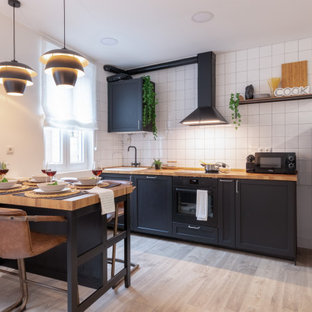 Ejemplo de cocina comedor lineal, actual, pequeña, con fregadero encastrado, armarios estilo shaker, puertas de armario negras, encimera de madera, salpicadero blanco, salpicadero de azulejos de porcelana, electrodomésticos negros, suelo gris y encimeras beige