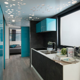 Diseño de cocina de galera, contemporánea, con fregadero encastrado, armarios con paneles lisos, puertas de armario negras, salpicadero negro, suelo de madera clara, suelo beige y encimeras blancas