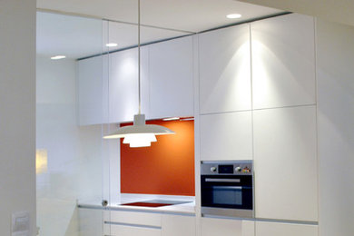 Foto på ett mellanstort funkis kök, med en undermonterad diskho, släta luckor, vita skåp, bänkskiva i kvarts, orange stänkskydd, fönster som stänkskydd, integrerade vitvaror, laminatgolv och brunt golv