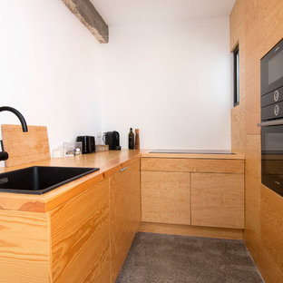 Diseño de cocina en U, urbana, cerrada, sin isla, con fregadero encastrado, armarios con paneles lisos, puertas de armario de madera oscura, encimera de madera, salpicadero blanco, electrodomésticos negros, suelo de cemento, suelo gris y encimeras marrones