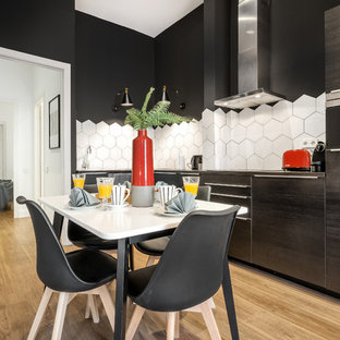 Ejemplo de cocina comedor en L, actual, de tamaño medio, sin isla, con armarios con paneles lisos, puertas de armario negras, salpicadero blanco, salpicadero de azulejos de cerámica, electrodomésticos negros, suelo laminado, encimera de acero inoxidable, suelo beige y encimeras grises