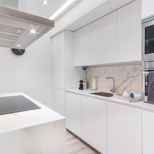 Ejemplo de cocina de galera, contemporánea, con fregadero bajoencimera, armarios con paneles lisos, puertas de armario blancas, electrodomésticos de acero inoxidable, suelo de madera clara, una isla, suelo beige y encimeras blancas
