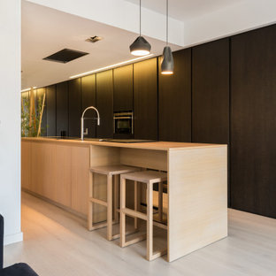 Imagen de cocina de galera, actual, grande, con fregadero encastrado, armarios con paneles lisos, puertas de armario negras, encimera de madera, electrodomésticos con paneles, una isla, suelo beige y encimeras beige