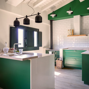 Diseño de cocina en U, tradicional renovada, con fregadero bajoencimera, armarios con paneles empotrados, puertas de armario verdes, salpicadero blanco, salpicadero de azulejos tipo metro, electrodomésticos con paneles, suelo de madera clara, península, suelo beige y encimeras blancas