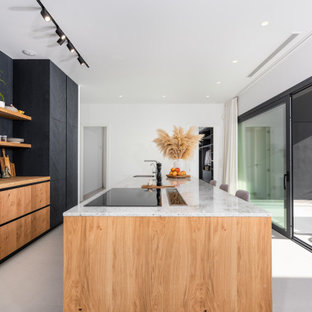 Modelo de cocina de galera, actual, extra grande, con fregadero bajoencimera, armarios con paneles lisos, puertas de armario negras, encimera de madera, electrodomésticos con paneles, una isla, suelo gris y encimeras beige