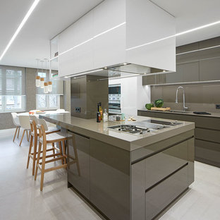 Imagen de cocina comedor en L, actual, con fregadero bajoencimera, armarios con paneles lisos, puertas de armario grises, salpicadero verde, electrodomésticos con paneles, una isla, suelo gris y encimeras grises