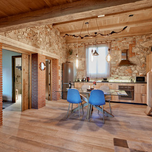 Imagen de cocina lineal, rural, abierta, con armarios con paneles lisos, puertas de armario de madera clara, electrodomésticos de acero inoxidable y suelo de madera clara